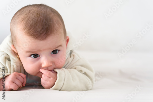 Portrait of an adorable smiling baby biting her own fingers putting her fist in her mouth.