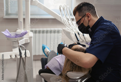 Mature dentist working with the beatiful young female patient in a modern hospital. Dentistry treatment in clinic and teeth hygiene