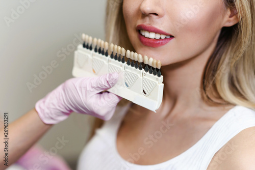 White teeth and beautiful smile of a young woman. Matching the shades of the implants using shade guide. Preparation for teeth whitening in dental office. Closeup macro white background isolated