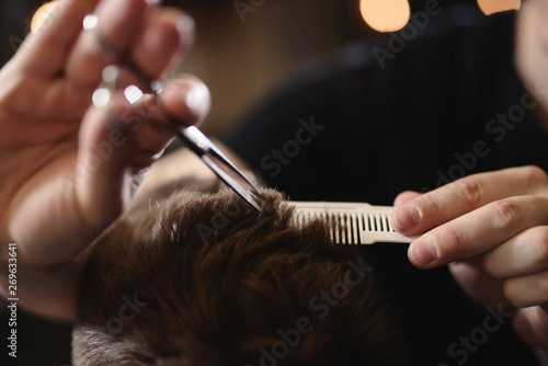 Close up barber's hands cuts hair with scissors and beard of men in the barbershop, hairdresser makes hairstyle for a young man