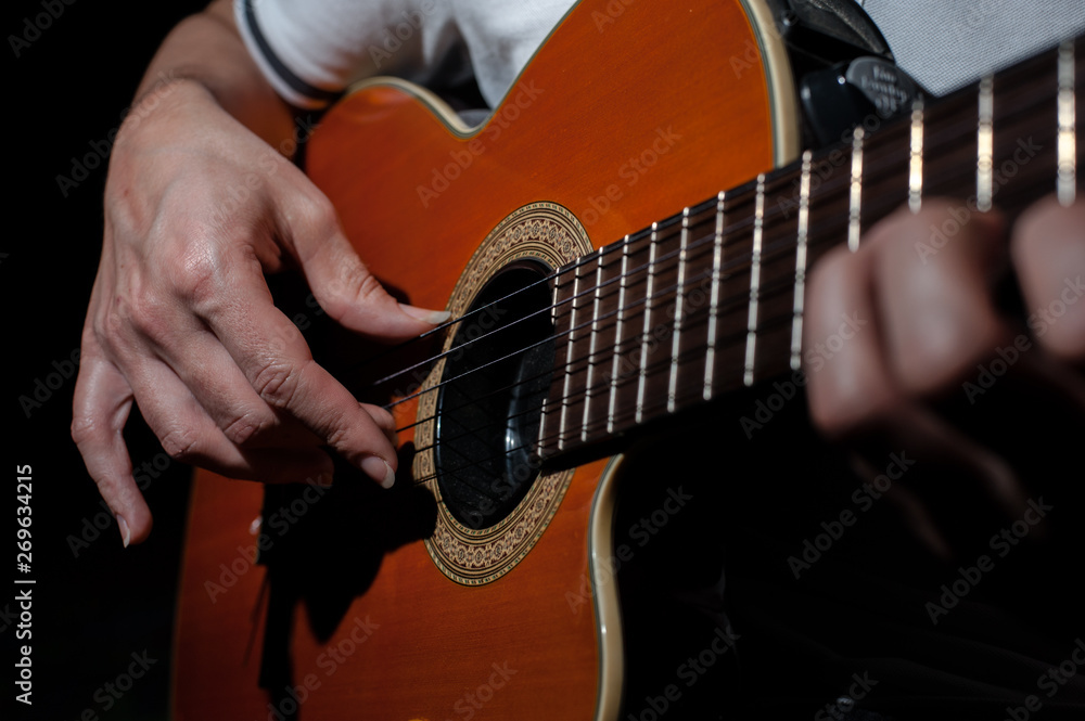 Fototapeta premium Man playing an acoustic guitar on a dark background. Playing guitar
