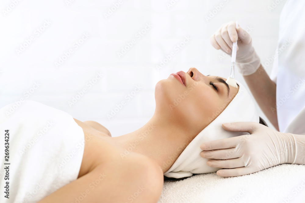 Obraz premium Model in white headband bandage cap lying on couch with closed eyes. Hand of beautician doctor in white glove touching her face with brush. Head and shoulders, healthcare, cosmetology, beauty clinic