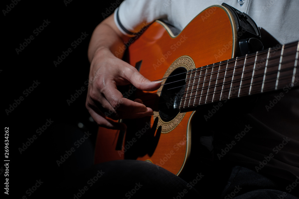 Fototapeta premium Man playing an acoustic guitar on a dark background. Playing guitar