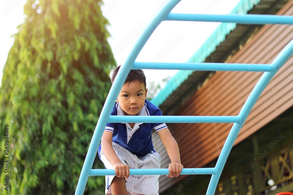 Obraz premium Happy asian child boy playing and climbing a steel bar toy at the playground. Kid and sport concept.