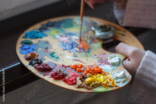 Close-up of female hands mixing paints on a palette with a spatula creating an oil painting