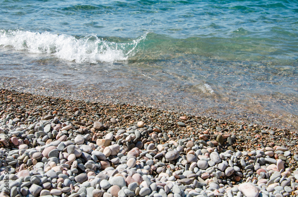 Summer background. Colorful coast with sea wave. View of the pebble beach and clear turquoise water