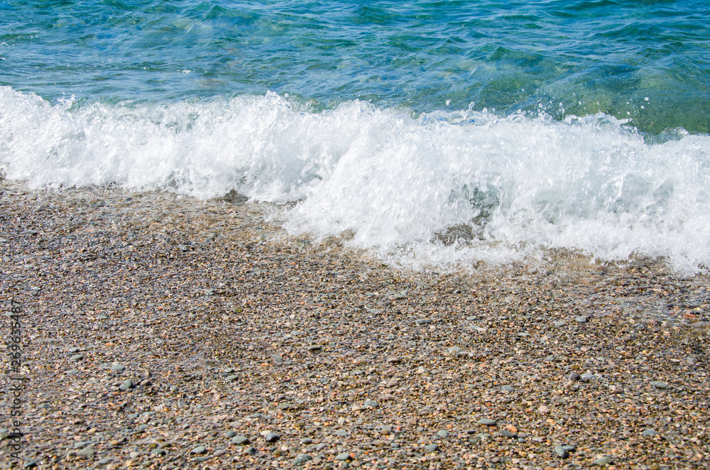 Summer background. Colorful coast with sea wave. View of the pebble beach and clear turquoise water Summer background. Colorful coast with sea wave. View of the pebble beach and clear turquoise water