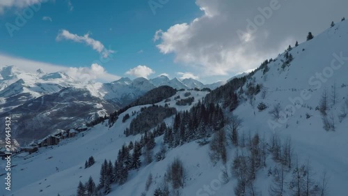 Drone flying at high altitude over snowy mountain slopes. Buildings of a ski resort barely visible in the distance. Winter wonderland and skiers paradise. photo