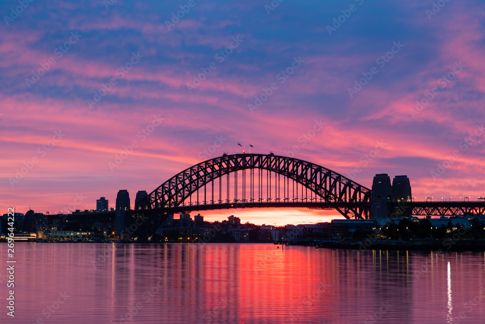 Silhouette of Sydney Harbour Bridge with colorful sky at dawn.