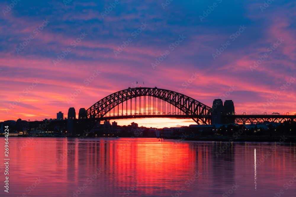 Silhouette of Sydney Harbour Bridge with colorful sky at dawn.