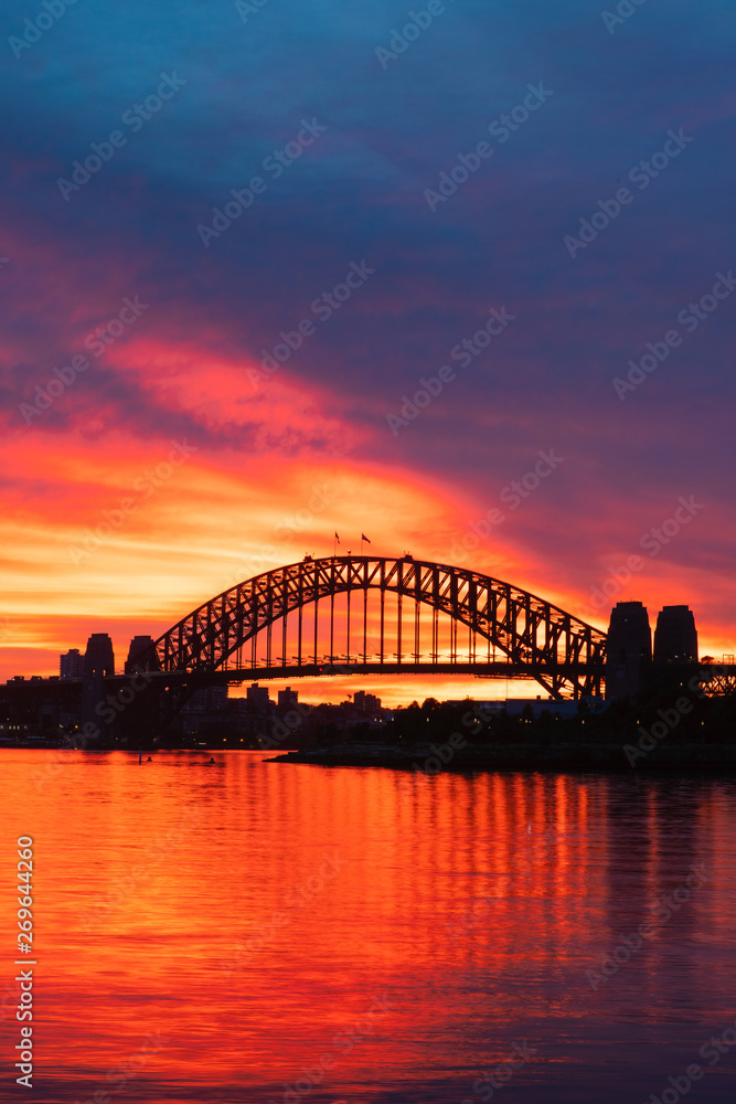 Silhouette of Sydney Harbour Bridge with orange burning sky at dawn.