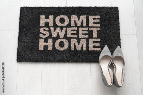 Modern condo businesswoman high heel shoes at home on entrance doormat saying Home Sweet Home welcoming homeowner after a day at work at new house background concept. Fashion grey suede kitten heels.