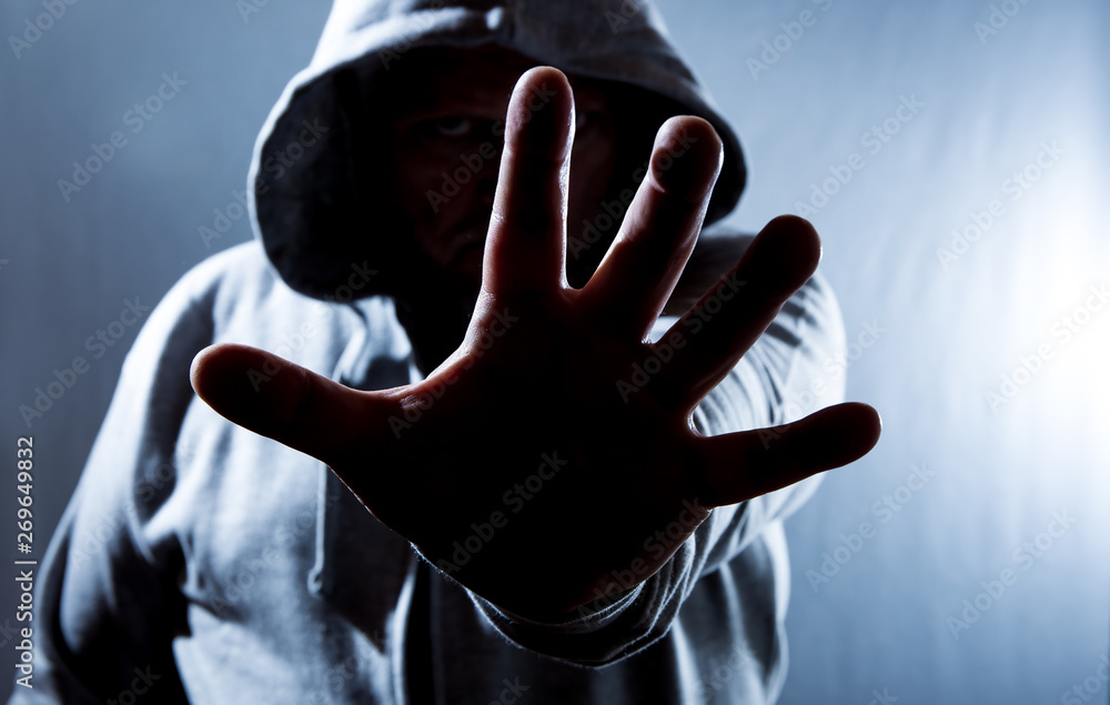 A hooded man holds his hand in front of his face defensively. Concept  self-defense. Photos | Adobe Stock