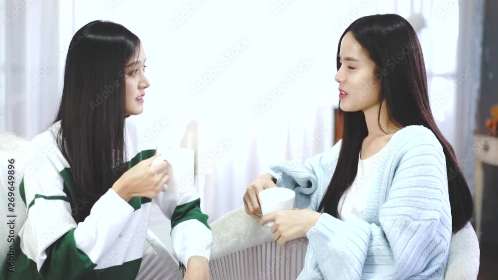 Happy female friends holding coffee mugs while discussing at table in living room relax time.Asian beauty woman smile and sititing sofa . Happy female friends holding coffee mugs while discussing at table in living room relax time.Asian beauty woman smile and sititing sofa .