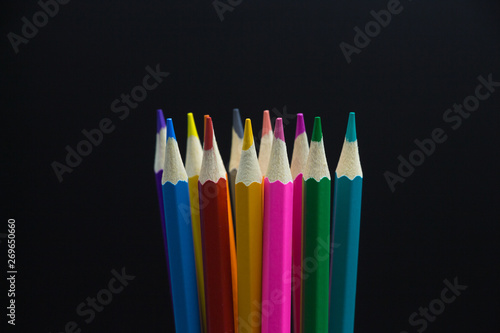 Close-up of a bunch of upright new colored pencils in the center of black background space