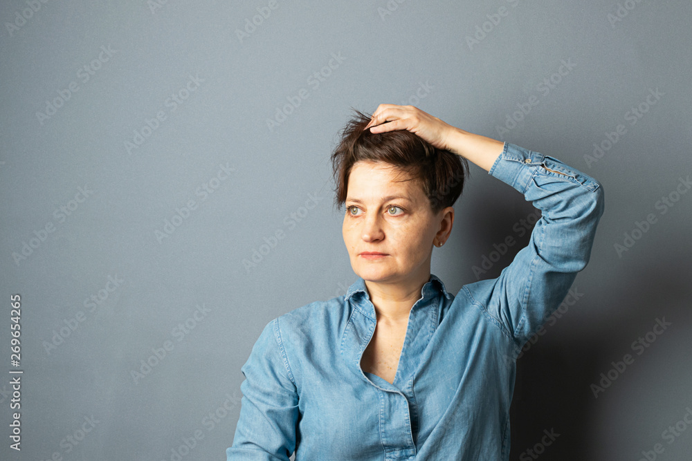 Portrait of a young woman with a short haircut that looks into the distance on a gray empty background. Human emotion Portrait of a young woman with a short haircut that looks into the distance on a gray empty background. Human emotion
