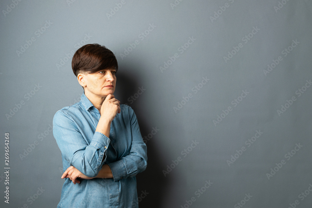 Portrait of a young woman with a short haircut on a gray blank background. Human emotions facial expression sadness