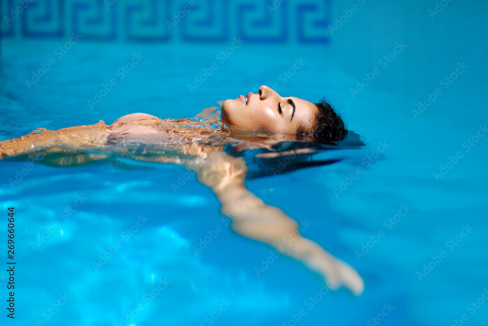 Beautiful tanned woman in bikini relaxing in swimming pool