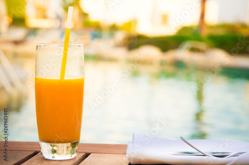 Glass of fresh mango juice on table near pool