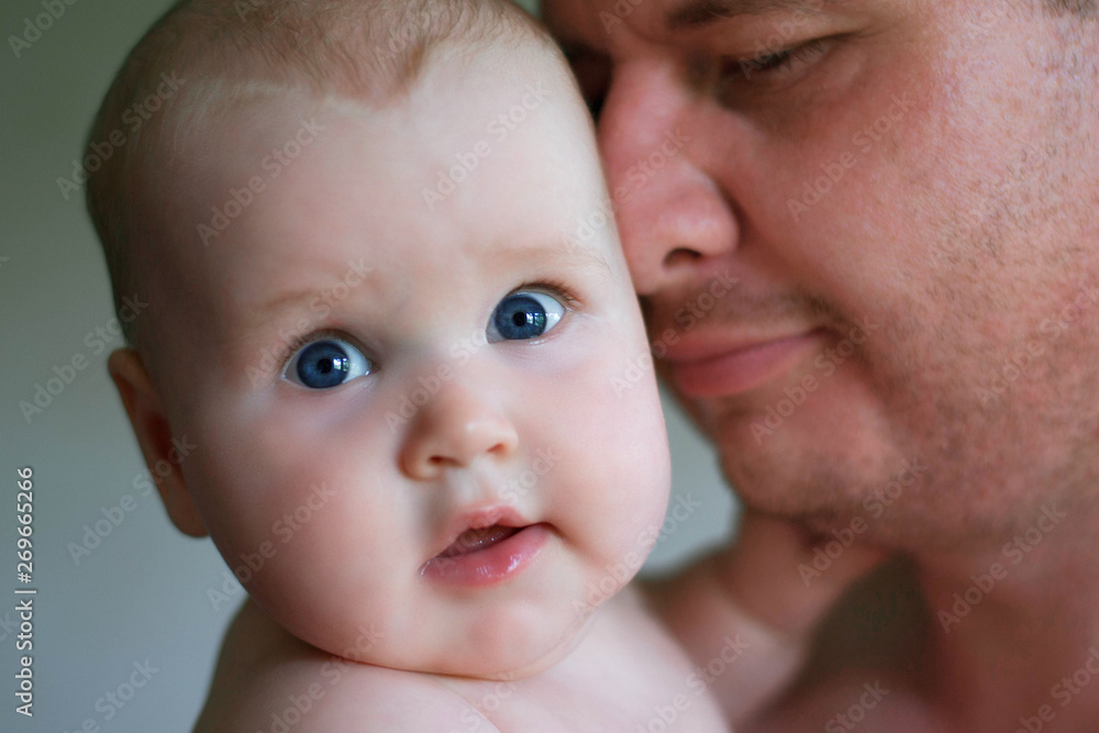 Portrait of a little girl, 5 months old and dad. A girl in her father's arms. She is very funny, her eyes wide open. She looks into the camera. Portrait of a little girl, 5 months old and dad. A girl in her father's arms. She is very funny, her eyes wide open. She looks into the camera.