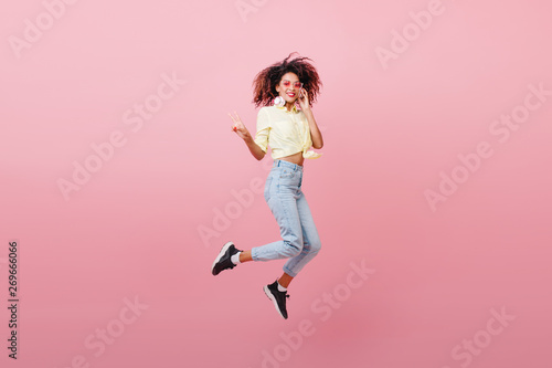 Spectacular sporty woman with brown skin dancing with happy face. Adorable black girl in black sneakers expressing positive emotions.