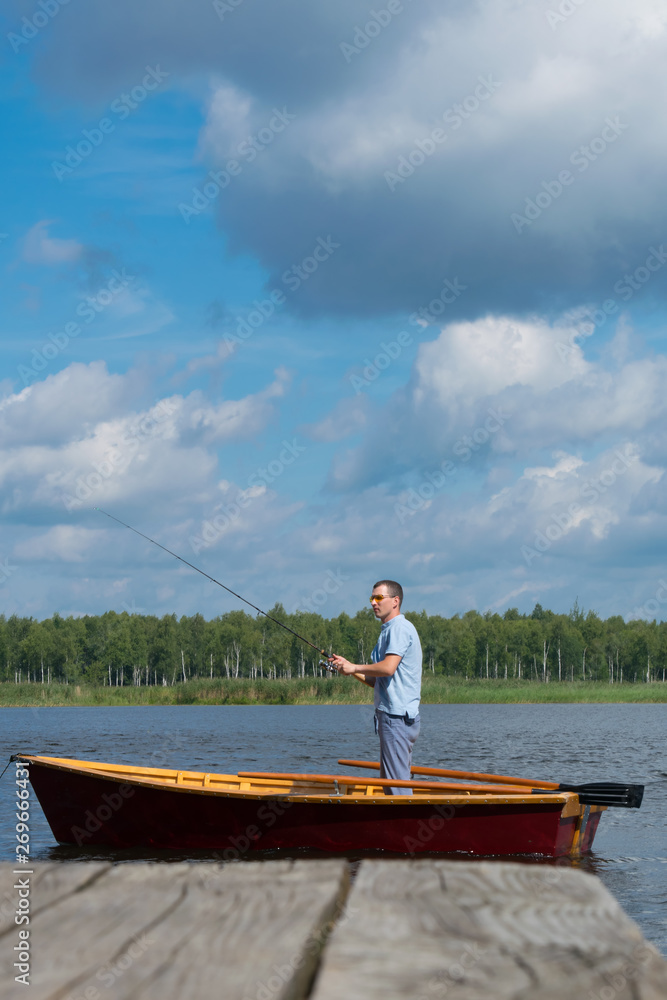 the man in the yellow glasses, the rowboat, holding a fishing rod and catches a fish on the background of the pier and the beautiful scenery