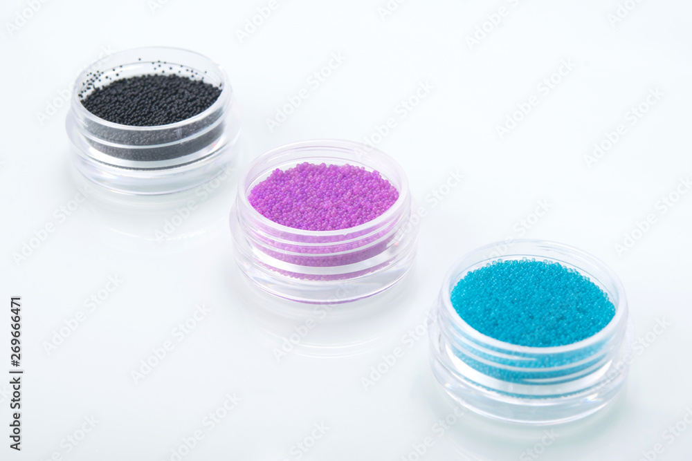 on a white background, close-up, in a row there are three containers with colorful nail decorations, decorative small balls on a white background, close-up, in a row there are three containers with colorful nail decorations, decorative small balls