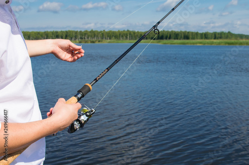close-up, a man holding a fishing rod and a hook for fishing, against the blue lake
