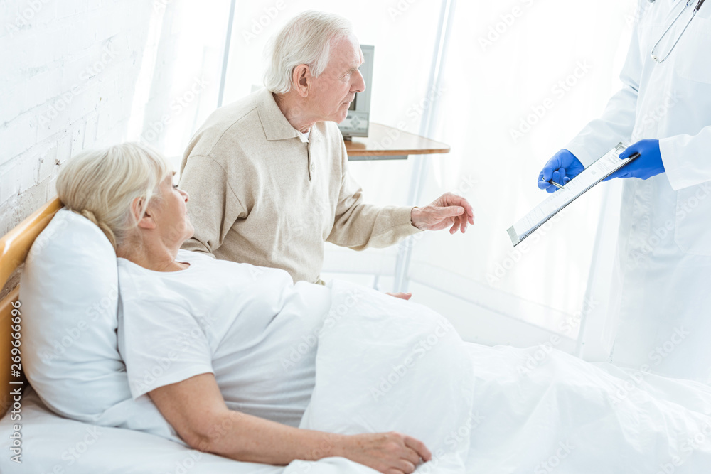 partial view of doctor holding clipboard, sick patient and senior man in clinic partial view of doctor holding clipboard, sick patient and senior man in clinic