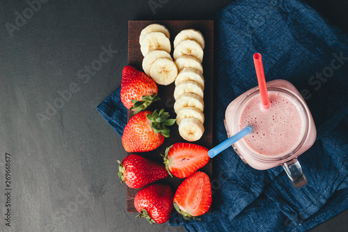 Smoothie with strawberry and banana in the jar at dark background, top view