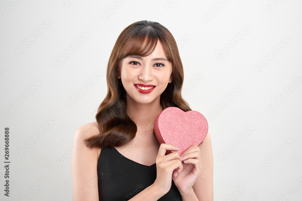 Cute young woman holding pink heart symbol against pale white background Cute young woman holding pink heart symbol against pale white background