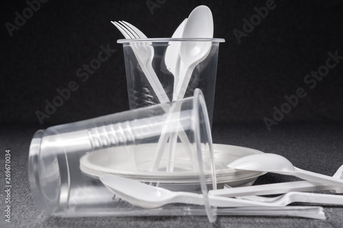 A set of plastic utensils. Plastic cups, plates, forks, spoons and plastic containers on a gray background. Against plastic