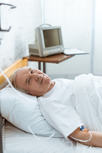 sick smiling senior man lying on bed in hospital