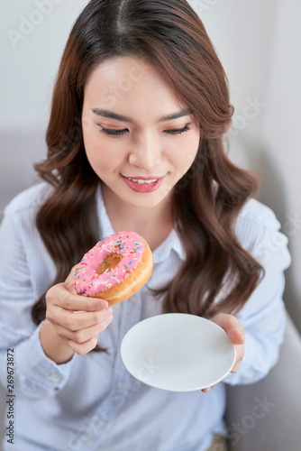 Portrait of beautiful young woman eating donuts at home.