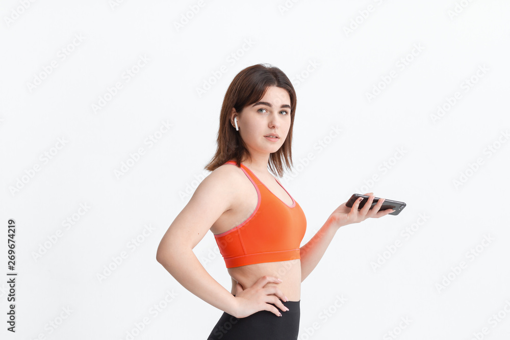 Young fitness woman posing isolated on a white background listening to music with wireless headphones.