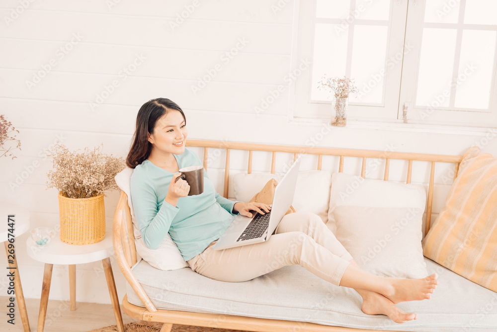 Happy casual beautiful woman working on a laptop sitting on the sofa in the house. Happy casual beautiful woman working on a laptop sitting on the sofa in the house.