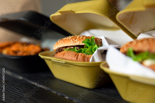 Hamburger in a takeaway container on the wooden background. Food delivery and fast food concept