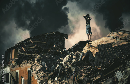 Homeless little boy watching destroyed houses and bombarded city. photo