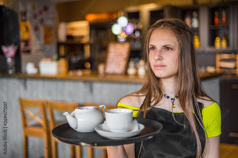 Portrait young waitress standing in cafe. girl the waiter holds in bunches a tray with utensils. Restaurant service Portrait young waitress standing in cafe. girl the waiter holds in bunches a tray with utensils. Restaurant service