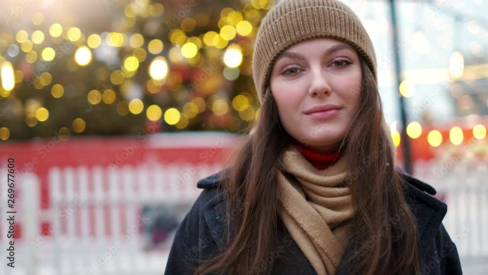 Pretty woman stands on the city square among Christmas decorations and looks straight into the camera Pretty woman stands on the city square among Christmas decorations and looks straight into the camera