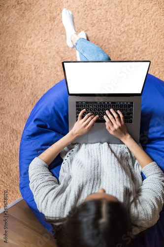 Top view of young woman cross-legged sitting on sofa working on laptop