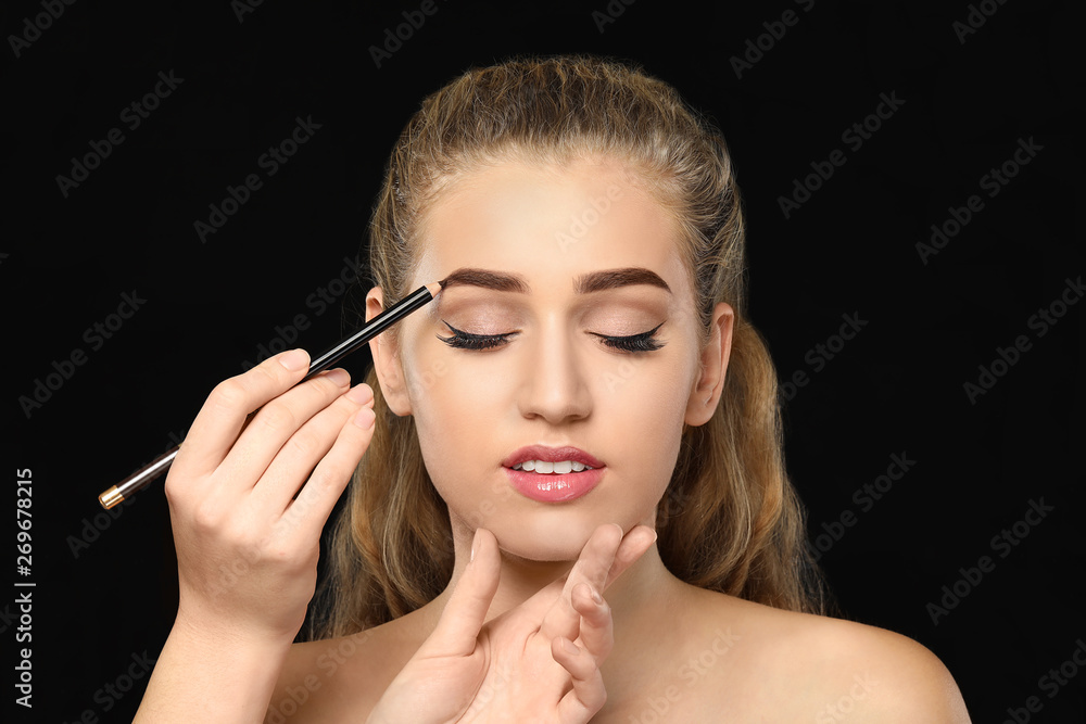 Fototapeta premium Young woman undergoing eyebrow correction procedure on dark background