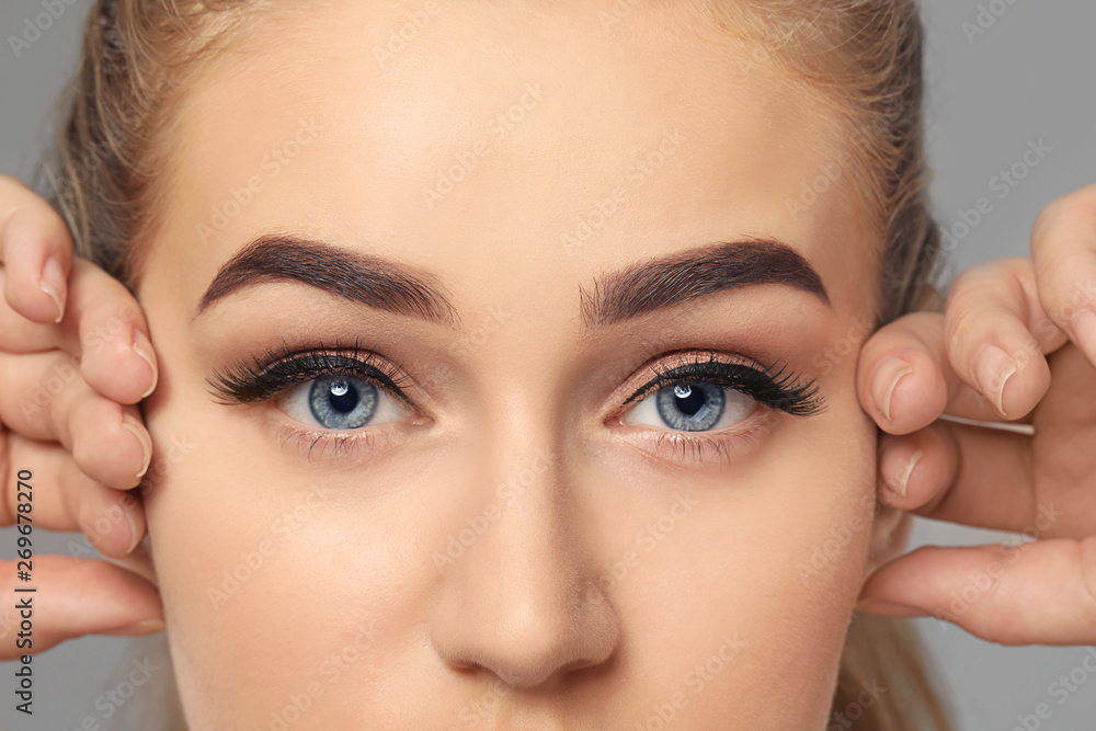 Fototapeta premium Young woman with beautiful eyebrows on grey background, closeup