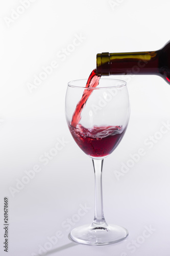 Pouring red wine into the glass on white background