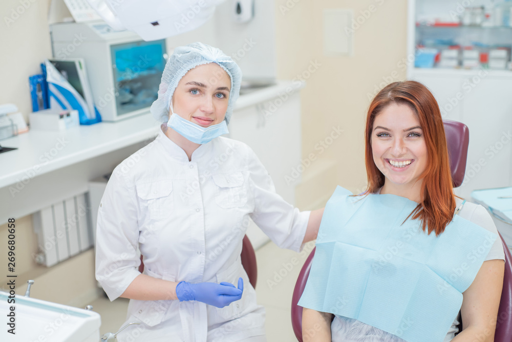 Obraz premium Young beautiful female dentist helps patient with toothache. Red-haired woman sits in a chair at the doctor on examination. Dental services.