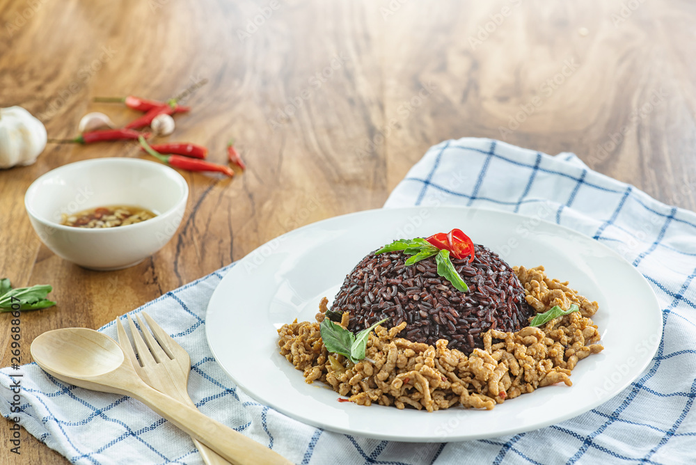 Stir fried basil with minced pork and berry rice in a plate on a wooden table. Stir fried basil with minced pork and berry rice in a plate on a wooden table.