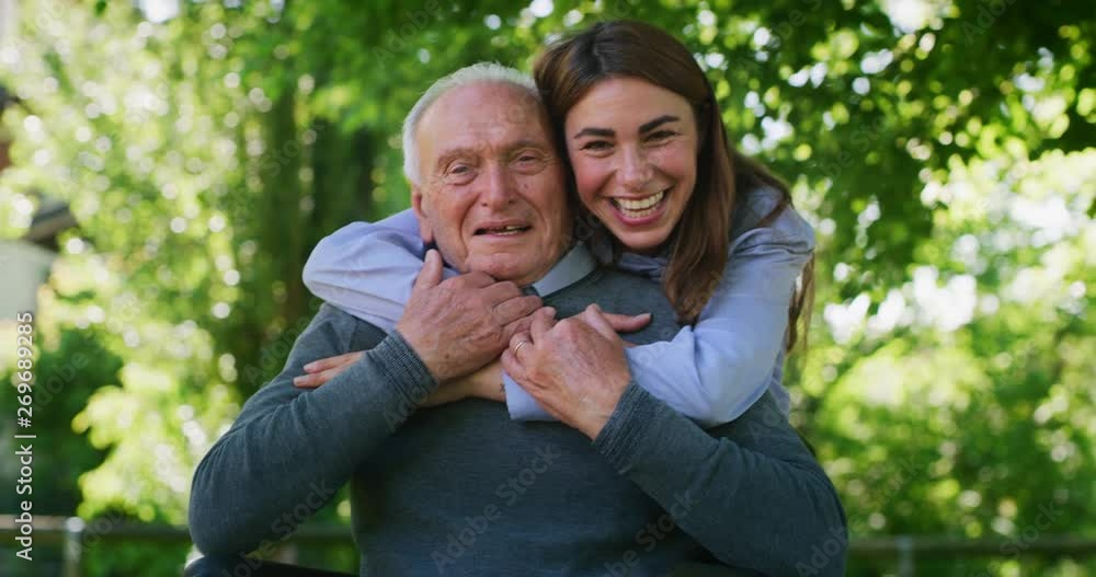 Slow motion of of happy granddaughter is hugging her grandfather in a wheelchair as a sign of love and respect in a green park on a sunny day. Slow motion of of happy granddaughter is hugging her grandfather in a wheelchair as a sign of love and respect in a green park on a sunny day.