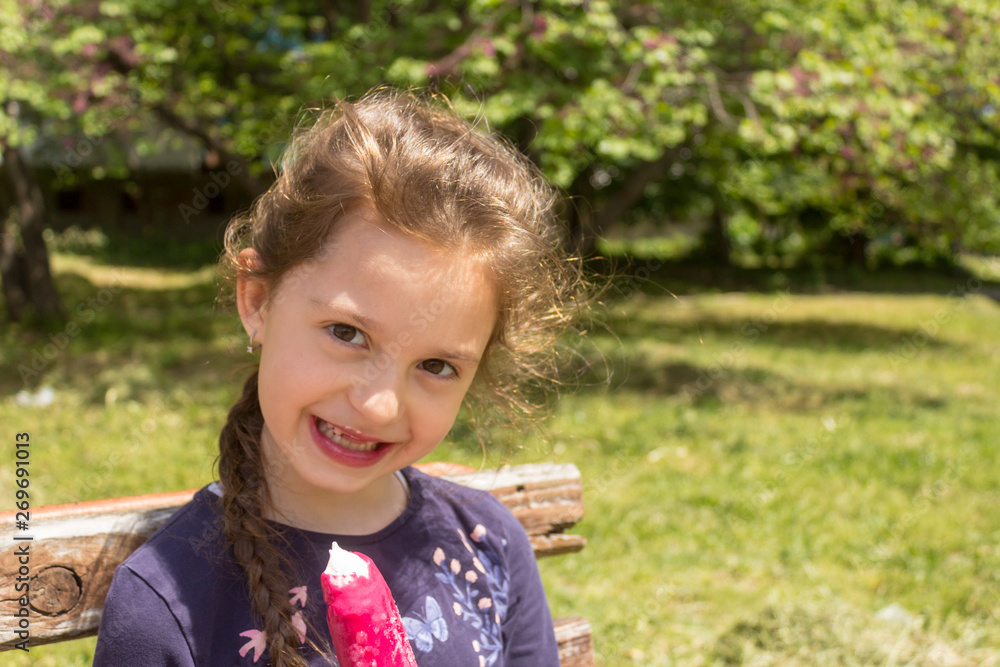 Pretty little girl eating an ice-cream sitting in a wooden bench. Pretty little girl eating an ice-cream sitting in a wooden bench.