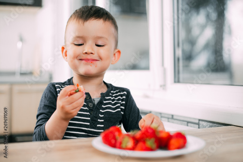 Little boy in the kitchen eating fresh strawberries very appetizing