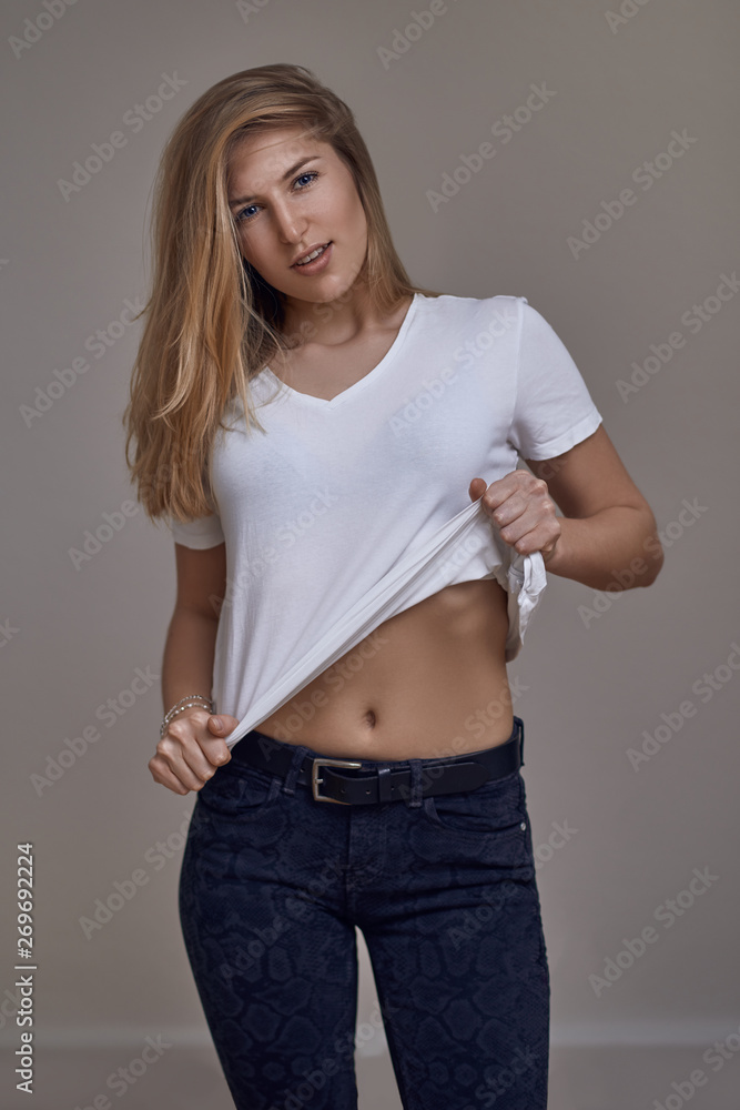 Attractive slender sexy young blond woman in jeans and a white T-shirt  lifting the corner